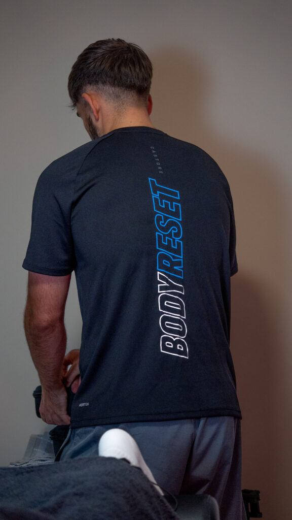 Sports massage Norwich therapist wearing a Body Reset branded t-shirt while preparing a treatment room for a professional sports massage session.